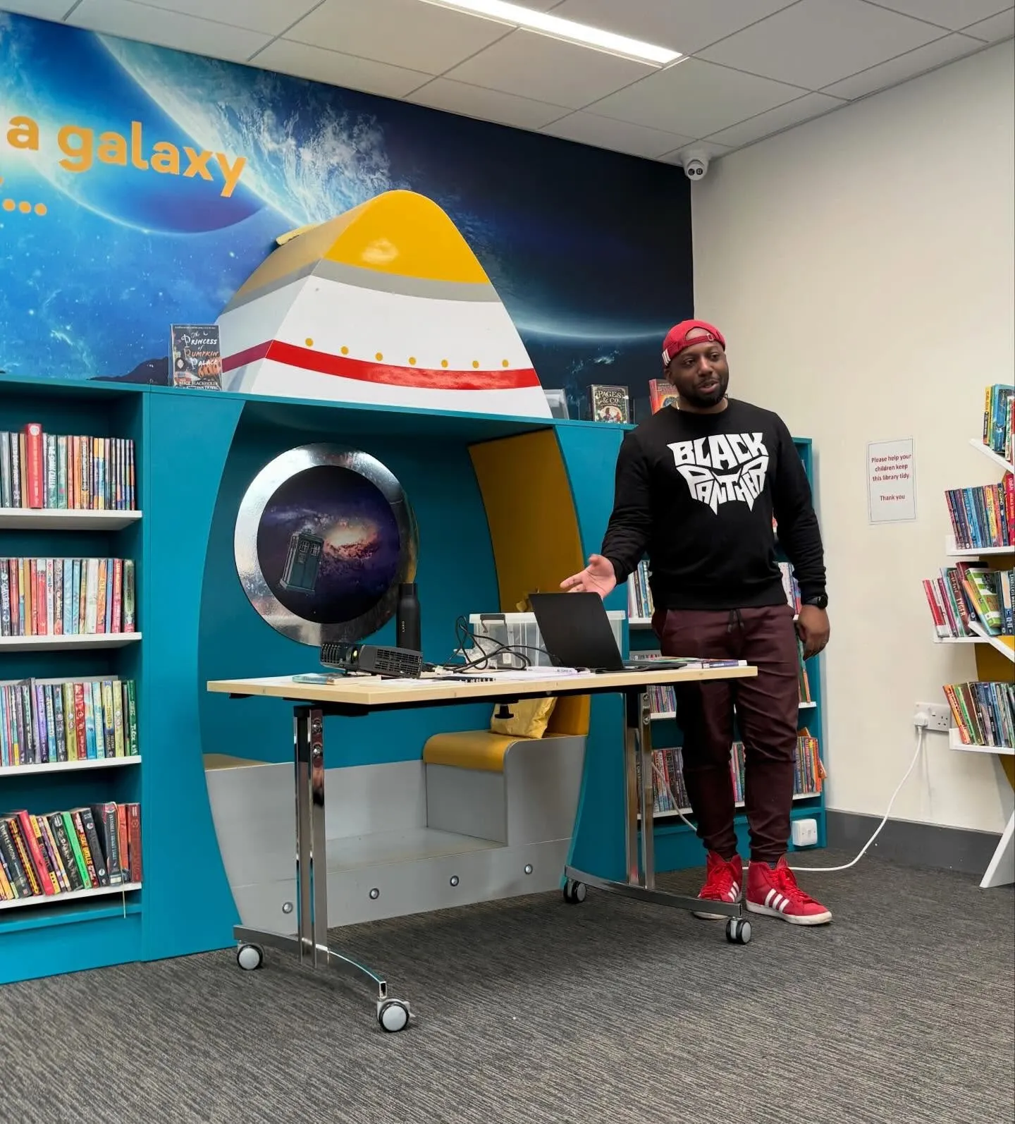 Ryan Crawford presenting in a library beside a rocket-shaped reading pod