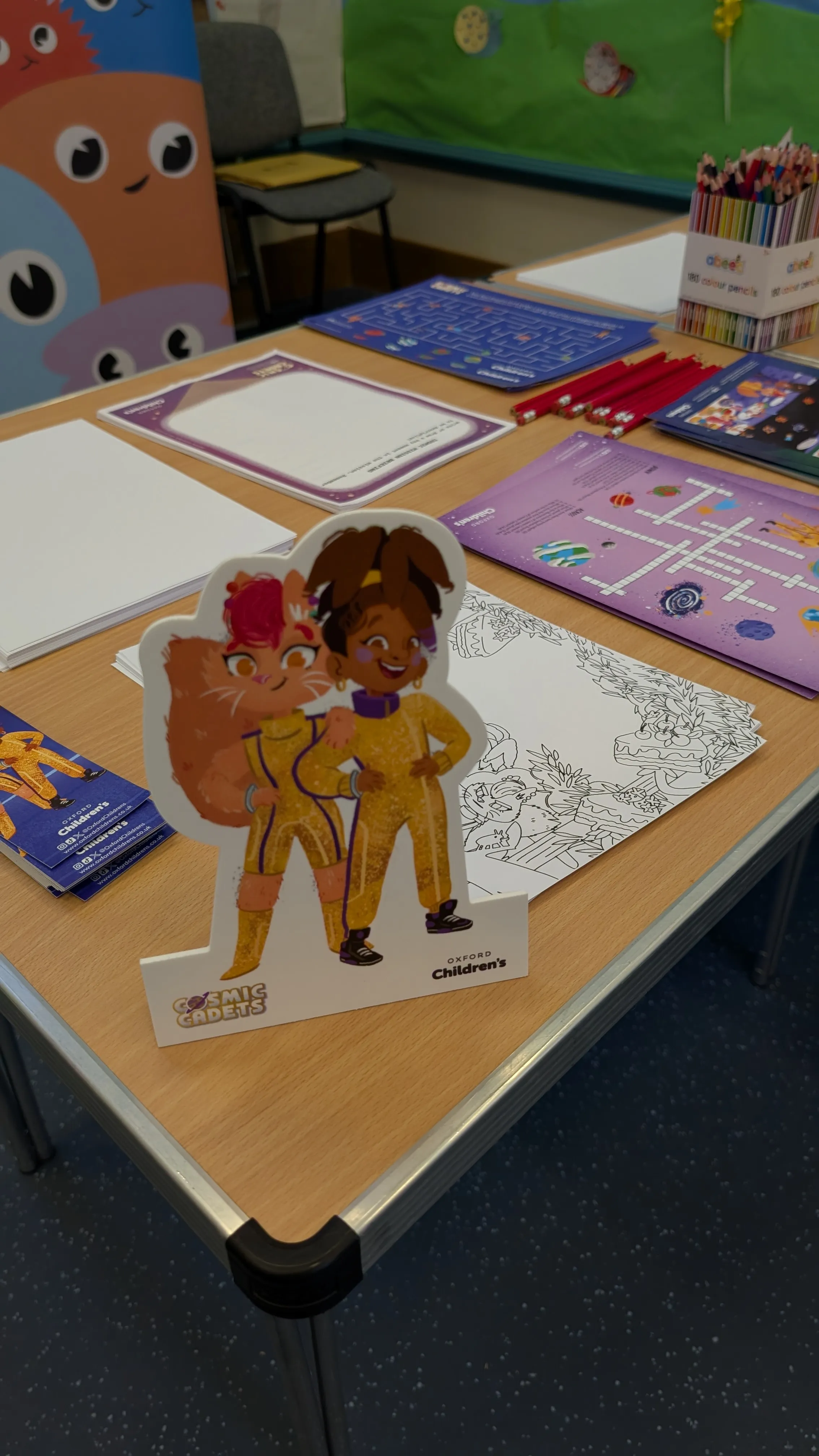 A Cosmic Cadets standee on a workshop table, colouring sheets and pencils laid out